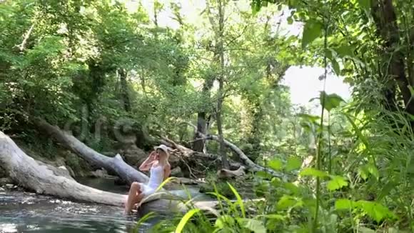 一个漂亮的女人坐在河边的一棵树上视频的预览图