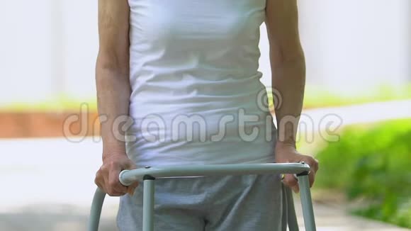 医院公园里一位手持步架的老妇人正对着镜头微笑恢复正常视频的预览图