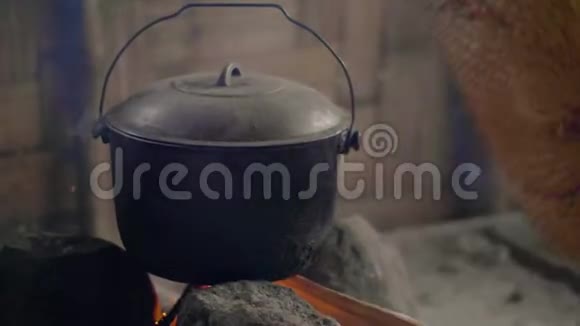 在篝火上用风扇吹火做饭准备传统火锅烧柴火的晚餐视频的预览图
