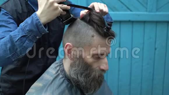 漂亮的女理发师用电动剃须刀和梳子把漂亮中年男子的头发剪成一条视频的预览图