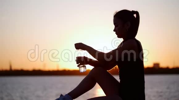 健康的年轻女运动员在日落时分运动后从塑料瓶中喝冷水视频的预览图