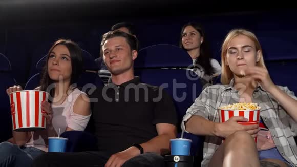 英俊的年轻男子在电影院拥抱两个女孩视频的预览图