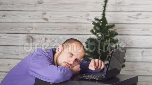 年夜在办公室里累得昏昏欲睡的商人办公室里的圣诞树桌子上有笔记本电脑商业概念男子视频的预览图