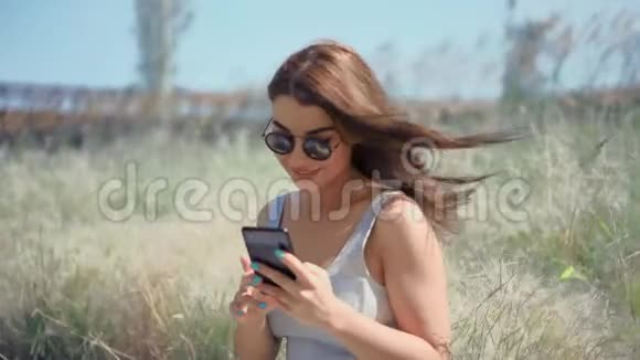 年轻的女人在阳光明媚的公园里用智能手机和朋友聊天视频的预览图