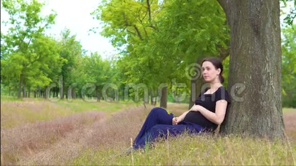 一个年轻漂亮怀孕的女孩穿着一件黑色T恤坐在树下视频的预览图