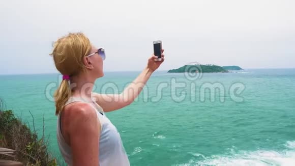 女孩游客在智能手机上拍摄大海和岛屿的照片热带旅行视频的预览图