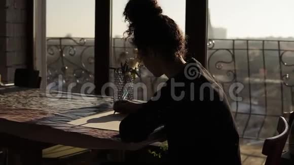 女艺术家坐在桌子旁桌上放着鲜花用笔在纸上画在一个极简约的艺术工作室里视频的预览图