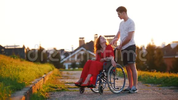 坐轮椅可爱的女孩在房子绿草和树木的背景上与她的年轻人交谈视频的预览图