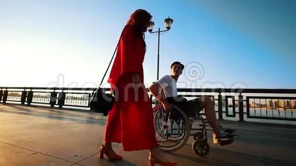 夏日傍晚一个年轻的残疾男子与一个美丽的女孩在海滨散步视频的预览图