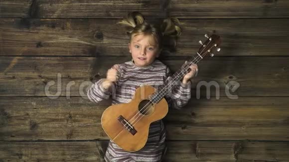 头顶上幸福的女孩在老式的木制背景上演奏四弦琴吉他文字或标志复制空间垂直顶部视图视频的预览图