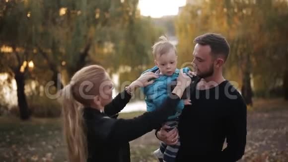 幸福的一家人在秋天公园湖边散步带着一个小儿子视频的预览图
