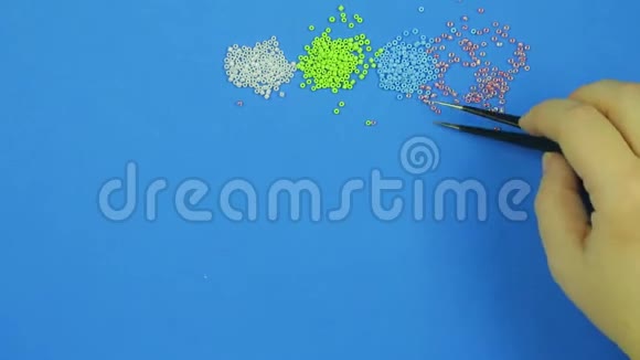 蓝色背景上的女性用镊子收集珠子特写视频的预览图