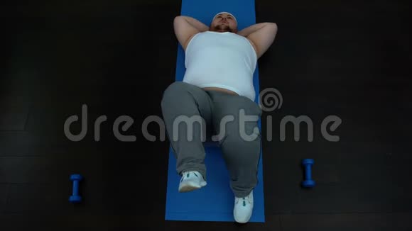 无动机的肥胖男性躺在垫子上做自行车运动减肥问题视频的预览图
