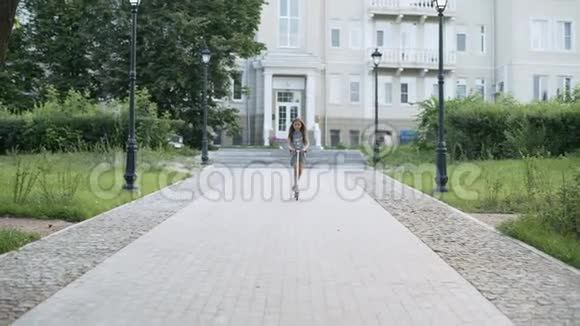 小女孩很快骑着踢踏板车沿着小路在夏天的乡村公园视频的预览图