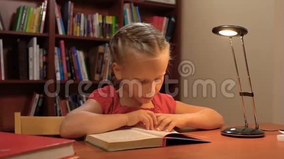 一个六岁的女孩坐在桌旁的台灯旁看书视频的预览图