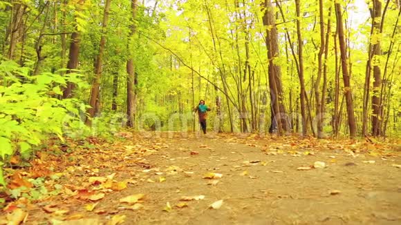 秋天公园里一个穿着外套和围巾的年轻女人手里拿着枫叶沿着小路跑视频的预览图