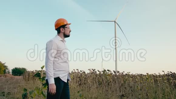 一位戴着橙色防护头盔和护目镜的工程师看着绿色领域的电力风力发电机之后视频的预览图