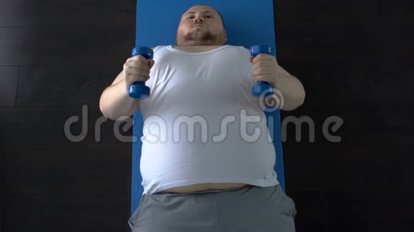 有目的的胖子举起哑铃努力躺在垫子上俯视视频的预览图