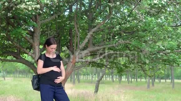 一个年轻美丽怀孕的女孩靠近一棵树穿着一件黑色T恤视频的预览图