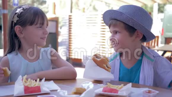 垃圾食品可爱的小男孩在街头咖啡厅喂女朋友汉堡视频的预览图