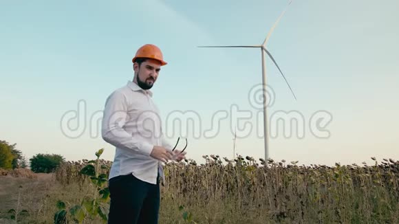 戴着橙色防护头盔的白种人工程师戴上护目镜看着风力发电机中的电力视频的预览图