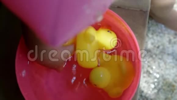 泰国芭堤雅2019年4月10日黄色塑料鸭子漂浮在粉红色的婴儿桶里一个孩子的手拿着一只鸭子视频的预览图