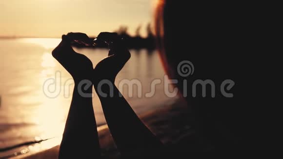 在海滩上日落的时候女人用她的手做心的象征慢动作电影风格视频的预览图
