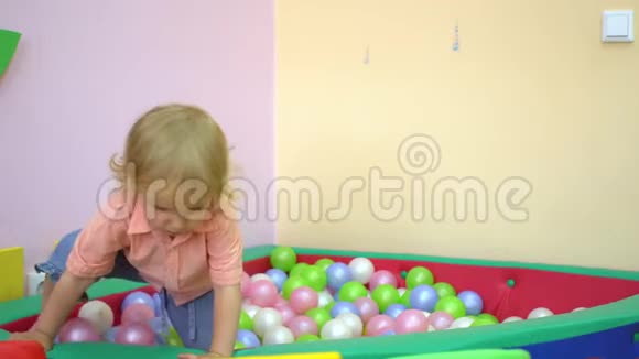 快乐可爱的宝贝女孩蹒跚学步跌到多种颜色的球池学前教育视频的预览图