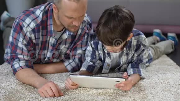 男孩在平板电脑上使用交互式应用程序在父亲的帮助下家庭时间视频的预览图