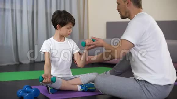 活泼的爸爸在家里教儿子做哑铃运动锻炼肌肉视频的预览图