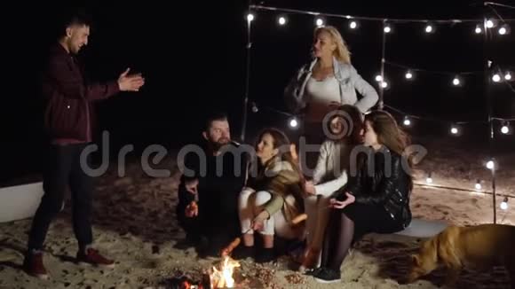 青春在夜晚的沙滩上休息用串串香肠在篝火旁猜单词视频的预览图