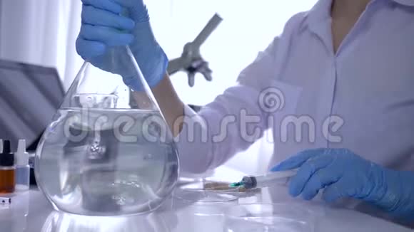 化学研究实验室助理用注射器将制剂注入大瓶中加水混合在明亮的地方视频的预览图