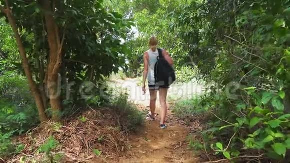 旅游女孩带着背包穿过雨林从小径上的树里出来热带岛屿视频的预览图