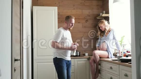 一位怀孕的妻子和丈夫在斯堪的纳维亚风格的厨房吃早餐坐在桌子上的孕妇视频的预览图
