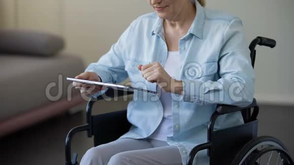 祖母坐在轮椅上在平板电脑上滚动着家庭照片视频的预览图