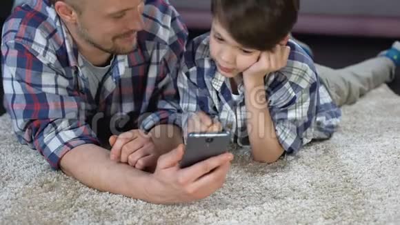 男孩和父亲在地板上玩智能手机游戏等妈妈下班视频的预览图
