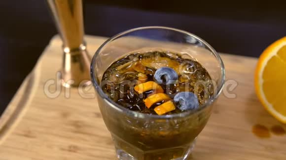 在岩石玻璃上的酒精鸡尾酒桌面上有橙色冰和蓝莓视频的预览图