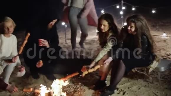 晚上年轻的朋友们坐在沙滩上生火一起用串烧香肠视频的预览图
