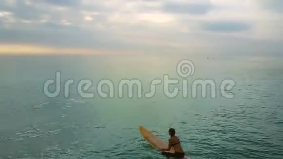 女孩躺在冲浪板上双手在海边的海洋上划桨视频的预览图