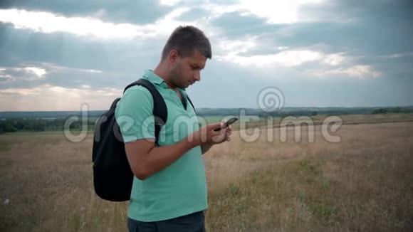 携带背包的年轻人使用智能手机数字设备模糊山顶背景触摸显示器视频的预览图