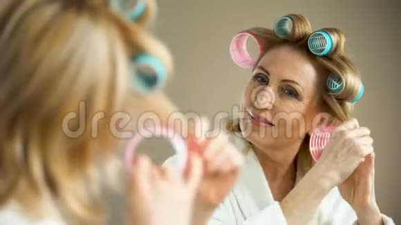 美丽的老太太把卷发器和微笑放进镜子里美容技巧视频的预览图