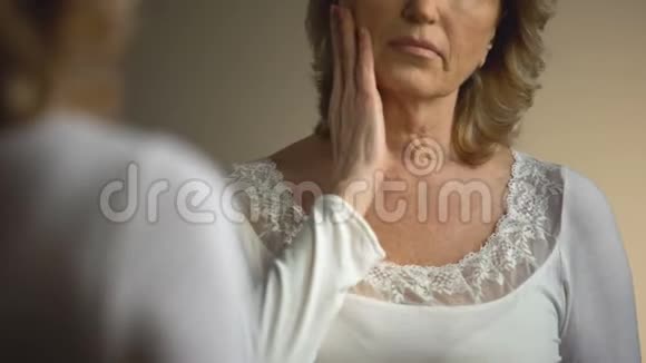 成熟的女性在镜子前摸着皱皱的脖子衰老过程视频的预览图
