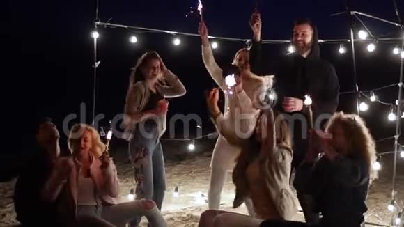 海滩派对朋友们在慢动作的灯泡背景上用孟加拉灯唱歌跳舞视频的预览图