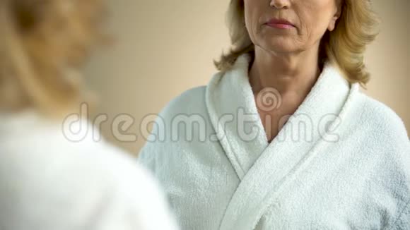 不高兴的老太太对着镜子看着自己的脖子衰老的过程视频的预览图