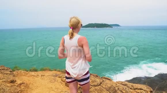 女人在看大海美丽的海景和一个岛屿海浪拍打着岩石视频的预览图