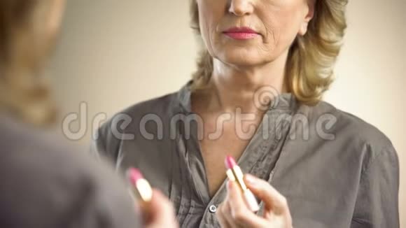 退休妇女在镜子前涂粉红色口红防老化妆品视频的预览图