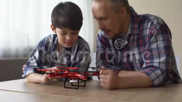好奇的父亲和小儿子在家里检查新的四翼飞机模型很有趣视频的预览图