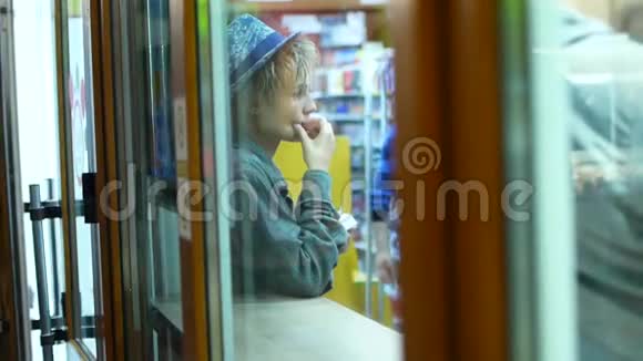 年轻漂亮的戴着帽子的女人在快餐店等他的食物从玻璃上看视频的预览图