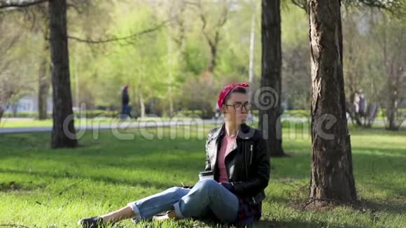 美丽年轻时尚的女人坐在公园的一棵树下喝着一杯咖啡大自然中的外卖咖啡时尚时尚时尚视频的预览图