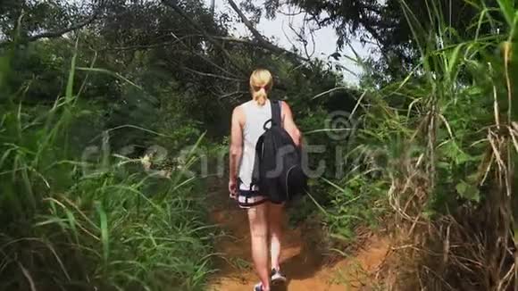 旅行者女孩带着背包沿着热带岛屿上的小径行走看着森林树木和大海美丽美丽视频的预览图